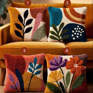 Könnte beinhalten: Vier dekorative Zierkissen mit farbenfrohen abstrakten und floralen Designs. Kissen zeigen eine Vielzahl von Formen, darunter Blätter, Kreise und Blumen, in den Farbtönen Orange, Blau, Lila und Grün. Die Kissen liegen auf einem gelben Sofa.