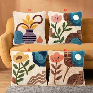 Puede incluir: Cuatro cojines decorativos con diseños florales y abstractos. Cada cojín presenta un fondo crema con patrones texturizados coloridos. Los diseños incluyen flores, jarrones y formas geométricas en tonos azules, naranjas, amarillos y marrones.