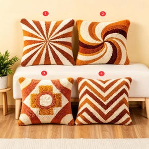 May include: Four square throw pillows with retro designs in shades of orange, brown, and cream. The patterns include a sunburst, a spiral, a geometric cross, and a chevron. The pillows are placed on a white bench.