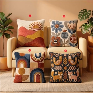 May include: Four square throw pillows with textured punch needle embroidery. Pillow 1 features a sun over hills. Pillow 2 displays blue and brown flowers. Pillow 3 shows geometric rainbow arches. Pillow 4 depicts foxes and birds on a dark background.