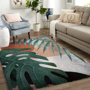 Peut inclure: Tapis rectangulaire avec un motif de feuilles tropicales. Le tapis présente de grandes feuilles de monstera vertes, avec des formes géométriques orange, pêche et blanches. Le tapis est placé dans un salon.