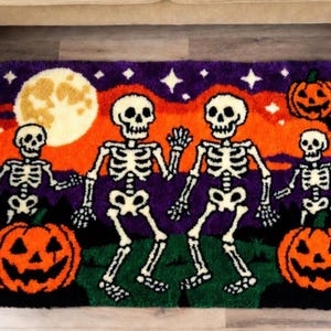Pode incluir: Tapete temático de Halloween com um design vibrante. Apresenta esqueletos dançando, abóboras, uma lua cheia e estrelas em um fundo roxo e laranja. O tapete é retangular e feito de um material macio.