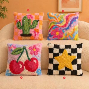 May include: Four decorative throw pillows with colorful, textured designs. One features a cactus, another a swirl of colors, a third has cherries, and the last a yellow star on a black and white checkered background. The pillows are square and appear to be handmade.