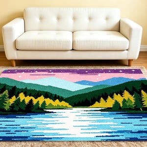 May include: A colorful area rug featuring a landscape design with a lake, mountains, and trees. The rug has a blue lake, green and yellow trees, and pink and purple sky. The rug is placed on a neutral-colored rug.