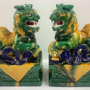 May include: A pair of green, yellow, and blue ceramic foo dogs. The foo dogs are sitting on square bases with intricate designs.