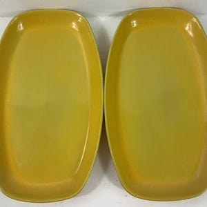 May include: Two yellow oval-shaped serving platters. The platters have a glossy finish and a slightly speckled appearance. The color is a bright, sunny yellow, and the platters are empty.
