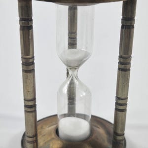 May include: An antique hourglass with a brass frame and clear glass. The hourglass has a round base and top, with four vertical supports. White sand is visible inside the glass, indicating the passage of time. A classic decorative item.