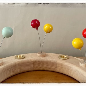 May include: A wooden advent calendar with five candle holders and five balloon decorations. The balloons are red, yellow, blue, and green.