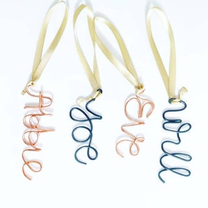 May include: Four wire ornaments with gold ribbon. The ornaments are in the shape of the names "Helen", "Hope", "Eve", and "Will". Two of the ornaments are copper wire and two are black wire.