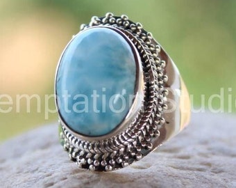 May include: A silver ring with a blue oval gemstone set in a decorative silver band. The ring is on a gray rock.
