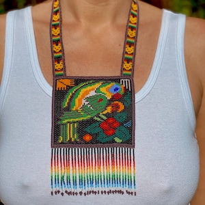 Puede incluir: Un collar de cuentas con un diseño de loro colorido y una franja arcoíris. El loro es verde, amarillo y azul, y las flores son rojas, naranjas y amarillas. La franja está hecha de pequeñas cuentas en un arcoíris de colores.