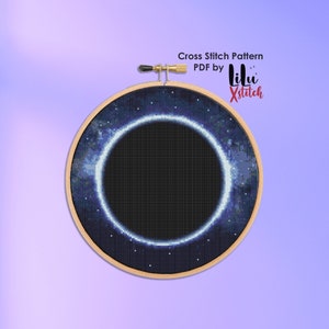 Puede incluir: Un patrón de punto de cruz de un agujero negro en el espacio. El patrón está en un aro de bordado de madera y está rodeado por una nebulosa azul y morada. El texto "Cross Stitch Pattern PDF by Lili Xstitch" está en la parte superior de la imagen.