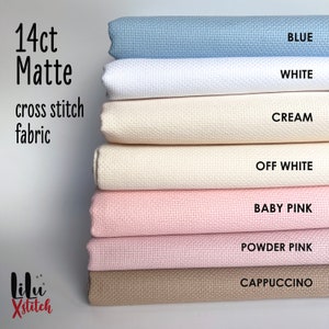 May include: A stack of 14 count Aida cloth fabric in various colors, including blue, white, cream, off-white, baby pink, powder pink, and cappuccino. The fabric is labeled "14ct Matte cross stitch fabric".