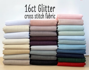 Può includere: Un mucchio di tessuto per punto croce glitterato da 16 fili in vari colori, tra cui bianco, beige, rosa, grigio, marrone, blu, verde e rosso. Il tessuto è disposto in una fila, con ogni colore impilato uno sopra l'altro. Il testo "16ct Glitter cross stitch fabric" è stampato sopra il tessuto.