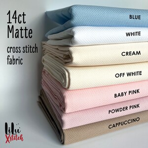 May include: A stack of 14 count Aida cloth in various colors, including blue, white, cream, off white, baby pink, powder pink, and cappuccino. The fabric is labeled "14ct Matte cross stitch fabric".