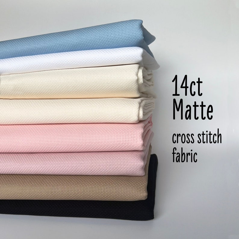 May include: A stack of 14 count matte cross stitch fabric in various colors, including blue, white, cream, pink, beige, and black. 14ct Matte cross stitch fabric.