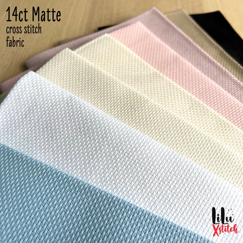 May include: A close-up of 14 count matte cross stitch fabric in a variety of colors, including white, beige, light blue, pink, and black. The fabric is folded in a stack, with the top layer showing the different colors. The text "14ct Matte cross stitch fabric" is visible at the top of the image.