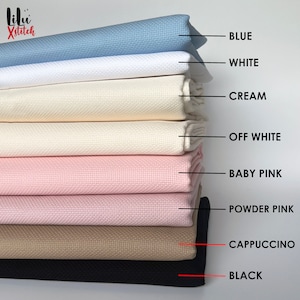 May include: A stack of eight Aida cloth fabric swatches in various colors, including blue, white, cream, off-white, baby pink, powder pink, cappuccino, and black. The fabric is a popular choice for cross-stitch projects.