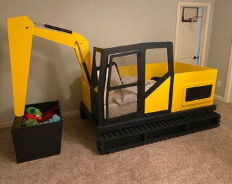 May include: A yellow and black toy excavator bed frame with a black metal mesh headboard and a black storage bin with stuffed animals. The bed frame has a black metal track base.
