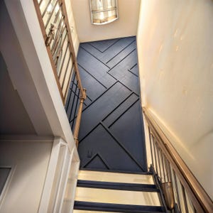 May include: A view of a staircase with a dark blue geometric patterned wall behind it. The wall is made of wood panels and has a chevron pattern. The staircase is made of wood and has a metal railing.