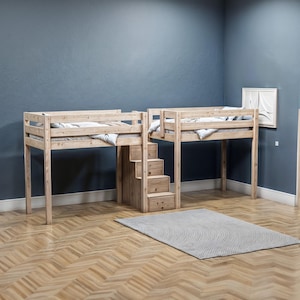 May include: Two wooden loft beds with a built-in ladder and drawers. The beds are made of natural wood and have a simple design. The beds are set up in a corner of a room with a light gray rug on the floor.