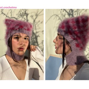 May include: A lilac-coloured, handmade, two-piece hat and neck warmer set. The hat features pointed ears and a checkered pattern in pink and red. The text "Brisa @bri.crochetmx" is visible in the top left corner.