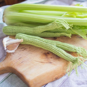 May include: A wooden cutting board with a green celery stalk, a knitted green celery stalk, and a clove of garlic.
