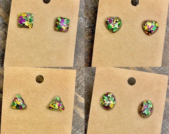 May include: Four pairs of stud earrings with different shapes, including square, heart, triangle, and circle. Each earring is filled with green, purple, and gold glitter.