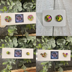 May include: Four sets of earrings featuring green, purple, and gold glitter. The earrings are displayed on white cards with the text "Glitter Me Happy by KT".