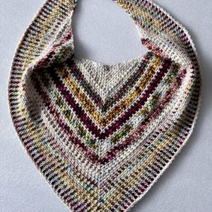 May include: A crocheted shawl with a triangular shape and a multi-coloured design. The shawl is made with a variety of shades of brown, pink, and green yarn.
