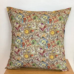 May include: Square decorative pillow with a repeating pattern of tarot cards in various colors. The cards feature illustrations and symbols, with a beige and brown background. The pillow is placed on a wooden surface.