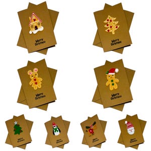 Op de afbeelding: Een verzameling kerstkaarten met feestelijke ontwerpen. Elke kaart heeft een ander applique, waaronder een peperkoekhuisje, kerstboom en kerstman. De woorden "Merry Christmas" staan op elke kaart.