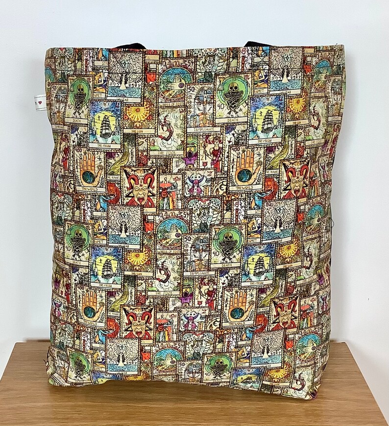 Op de afbeelding: Een tote bag met een kleurrijk ontwerp met een herhalend patroon van tarotkaarten. De kaarten zijn in verschillende kleuren en stijlen en zijn willekeurig gerangschikt. De tas is gemaakt van een duurzame stof en heeft twee handvatten.