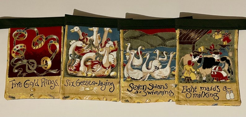 May include: A set of four fabric wall banners with a green border. Each banner features a different scene from the song "The Twelve Days of Christmas". The banners depict five gold rings, six geese a-laying, seven swans a-swimming, and eight maids a-milking.