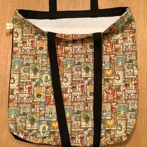 Op de afbeelding: Een beige tote bag met zwarte banden. De tas is gemaakt van canvas en heeft een patroon van kleurrijke illustraties.