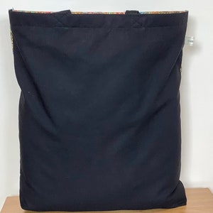 Op de afbeelding: Zwarte tote bag met een kleurrijke, gepatroneerde voering. De tas heeft twee handvatten en een label met de tekst "made".