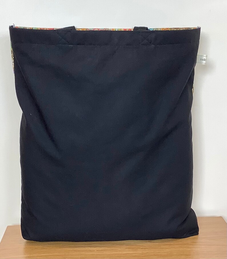 Op de afbeelding: Zwarte tote bag met een kleurrijke, gepatroneerde voering. De tas heeft twee handvatten en een label met de tekst "made".