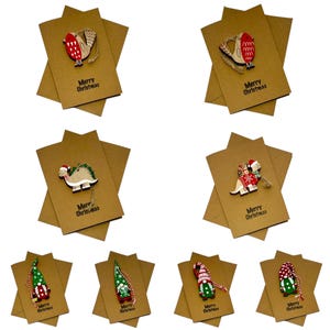 Op de afbeelding: Een verzameling kerstkaarten van kraftpapier met houten ornamenten. Elke kaart heeft een uniek ornament, waaronder een vogel, een dinosaurus en een kabouter. De woorden "Merry Christmas" staan op elke kaart.
