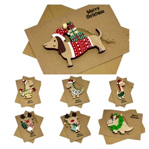 Op de afbeelding: Houten kerstversieringen met een teckel met een kerstmuts en trui, en diverse dinosaurussen en rendieren. Elk ornament zit op een stervormige kaart met de tekst "Merry Christmas" erop.