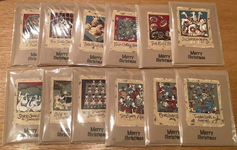 Op de afbeelding: Een verzameling kerstkaarten, elk afzonderlijk verpakt. De kaarten bevatten illustraties uit het lied "The Twelve Days of Christmas", met teksten als "Twee tortelduiven" en "Vrolijk Kerstfeest".