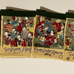 May include: A set of four fabric banners with illustrations of the 12 Days of Christmas. Each banner features a different verse of the song, with colorful illustrations of the gifts. The banners are sewn together with green ribbon.