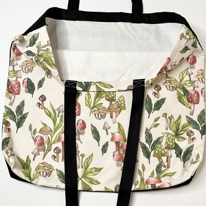 May include: A white tote bag with black straps and a mushroom print. The mushrooms are in shades of brown, red, and green.