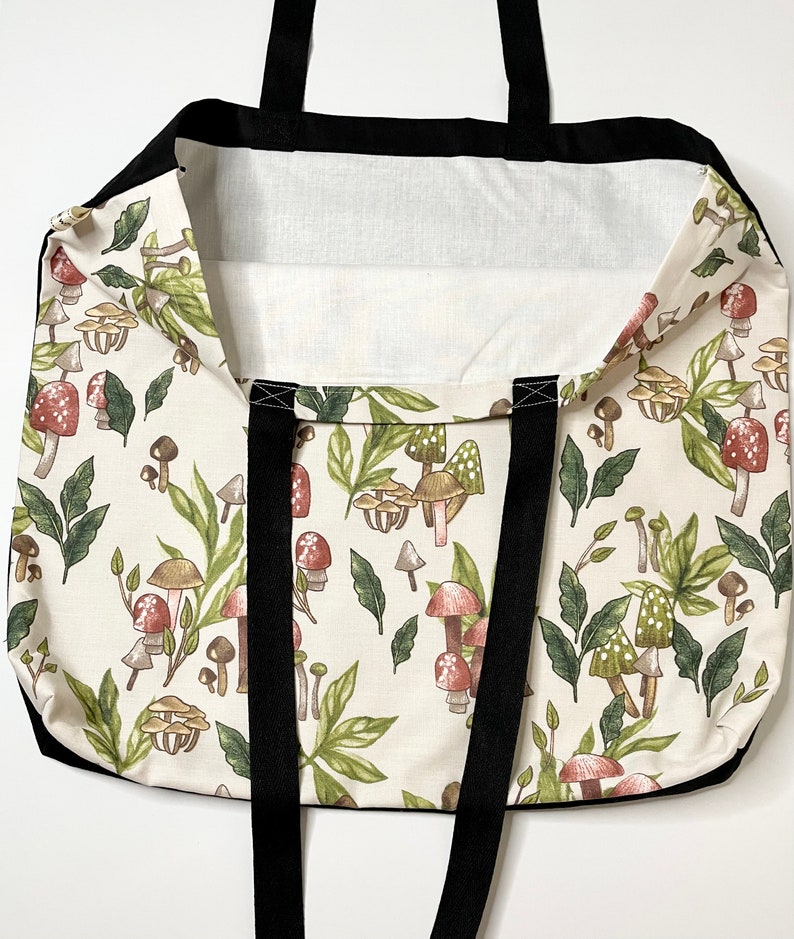 May include: A white tote bag with black straps and a mushroom print. The mushrooms are in shades of brown, red, and green.