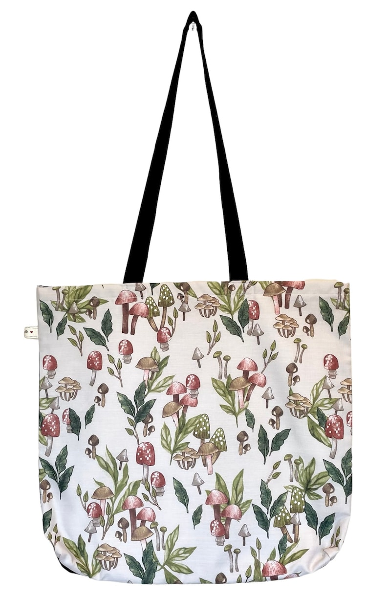 May include: A white tote bag with a black handle and a pattern of red and brown mushrooms and green leaves.