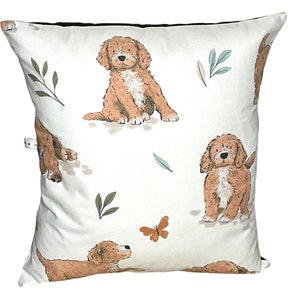 May include: A white throw pillow with a brown and white puppy dog pattern. The pillow features a repeating pattern of puppies with green leaves and a butterfly.