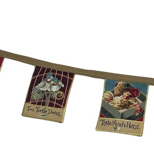 May include: A brown fabric banner with five colorful flags. Each flag features a different illustration and text. The flags read: "A Prairie in a Pear Tree", "Two Turtle Doves", "Three French Hens", "Four Calling Birds".