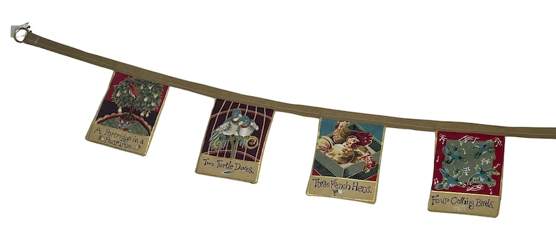 May include: A brown fabric banner with five colorful flags. Each flag features a different illustration and text. The flags read: "A Prairie in a Pear Tree", "Two Turtle Doves", "Three French Hens", "Four Calling Birds".