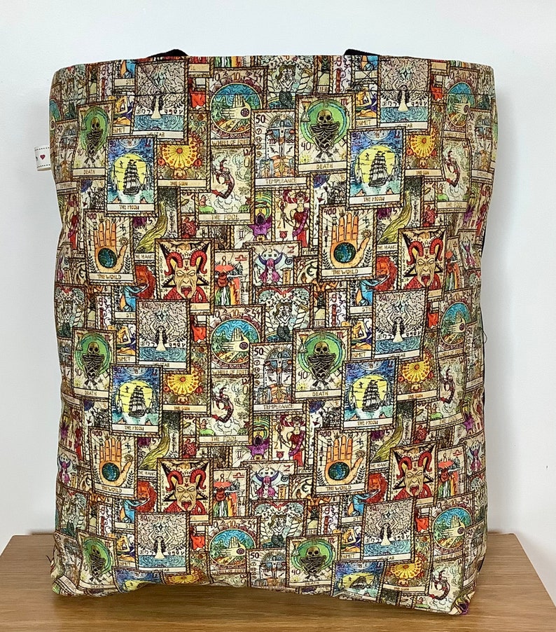 Op de afbeelding: Een beige tote bag met een kleurrijk patroon van tarotkaarten. De tas is gemaakt van stevige stof en heeft een groot hoofdvak.