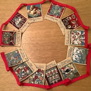 May include: A red and white string of bunting with 12 flags. Each flag has a different illustration and text. The text on the flags includes: "A Partridge in a Pear Tree", "Two Turtle Doves", "Three French Hens", "Four Calling Birds", "Five Gold Rings", "Six Geese a-Laying", "Seven Swans a-Swimming", "Eight Maids a-Milking", "Nine Ladies Dancing", "Ten Lords a-Leaping", "Eleven Pipers Piping", and "Twelve Drummers Drumming".