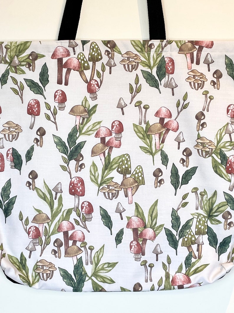 May include: White tote bag with a mushroom and leaf pattern. The mushrooms are red, brown, and white with green leaves.